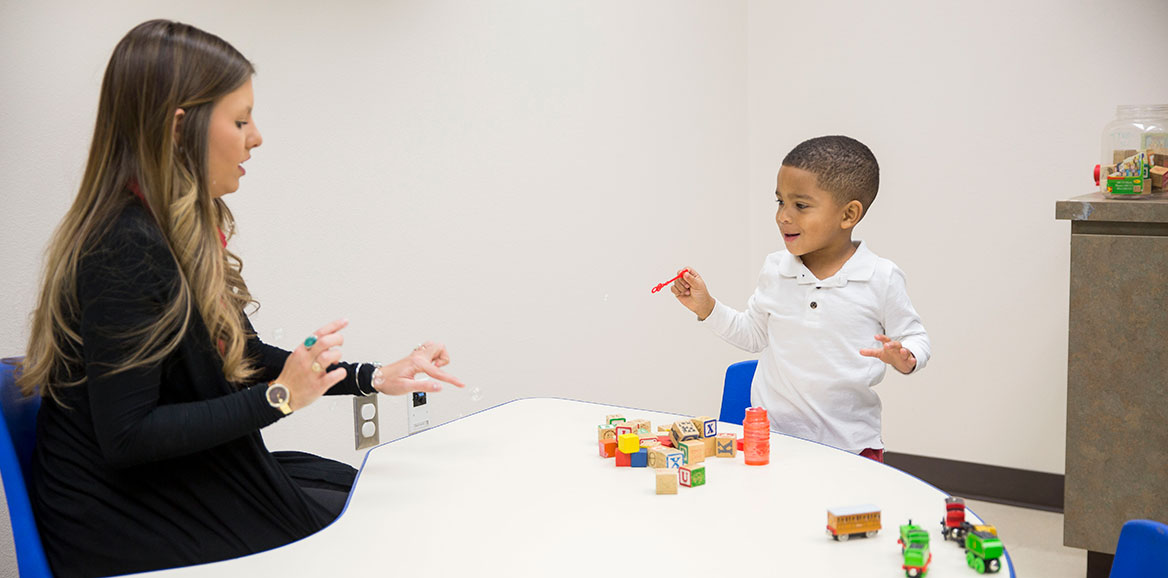 A Bachelor of Science in Speech, Language, and Hearing Sciences student uses bubbles and blocks to interact with a child.